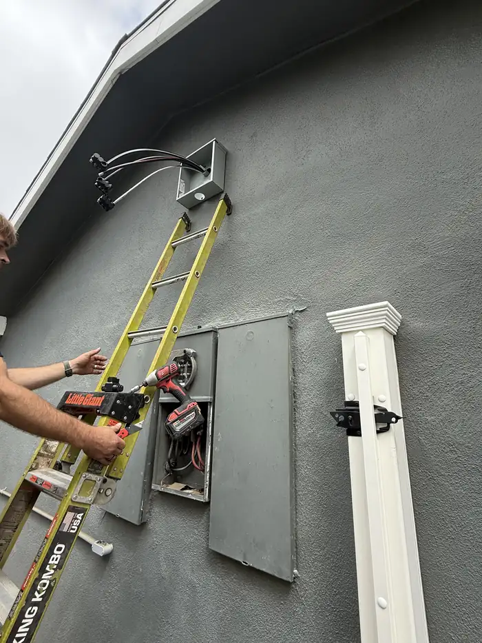 Pelican Coast electrician on a ladder working at a service entrance and weatherhead